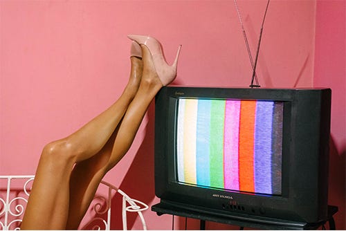 Womans legs rest on top of an old-fashioned T.V. in front of a pink wall Womans legs rest on top of an old-fashioned T.V. in front of a pink wall
