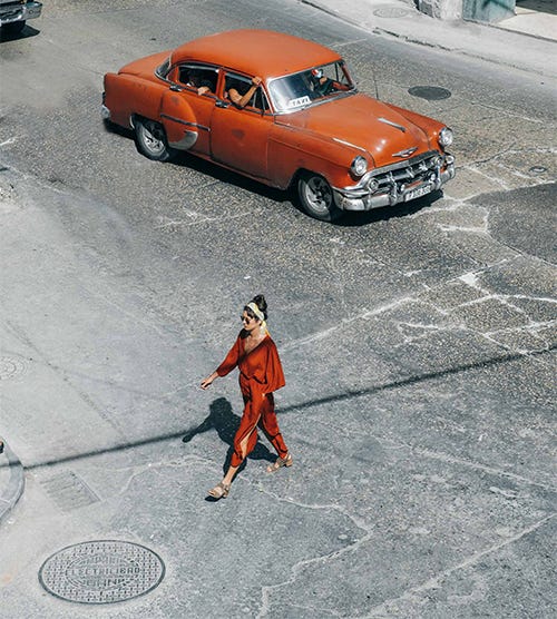 A woman dressed in orange crossing the street in front of a orange car A woman dressed in orange crossing the street in front of a orange car