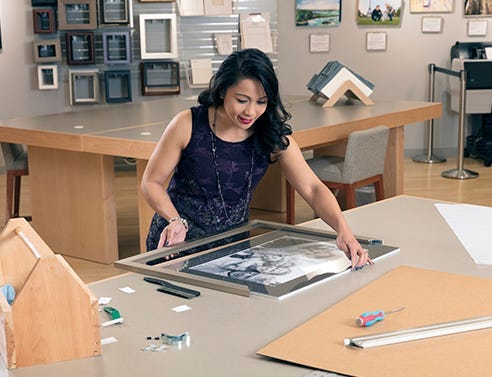 Woman with dark hair and purple shirt DIY framing her matted photograph with a silver metal frame