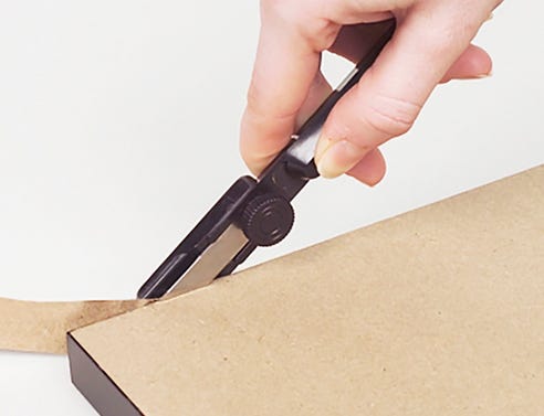 Woman's hand using the dust cover trimmer tool to trim the dust cover to the size of the wood frame