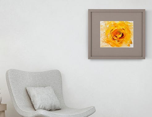 Yellow floral artwork framed with a grey mat and frame hanging on the wall above a grey armless chair